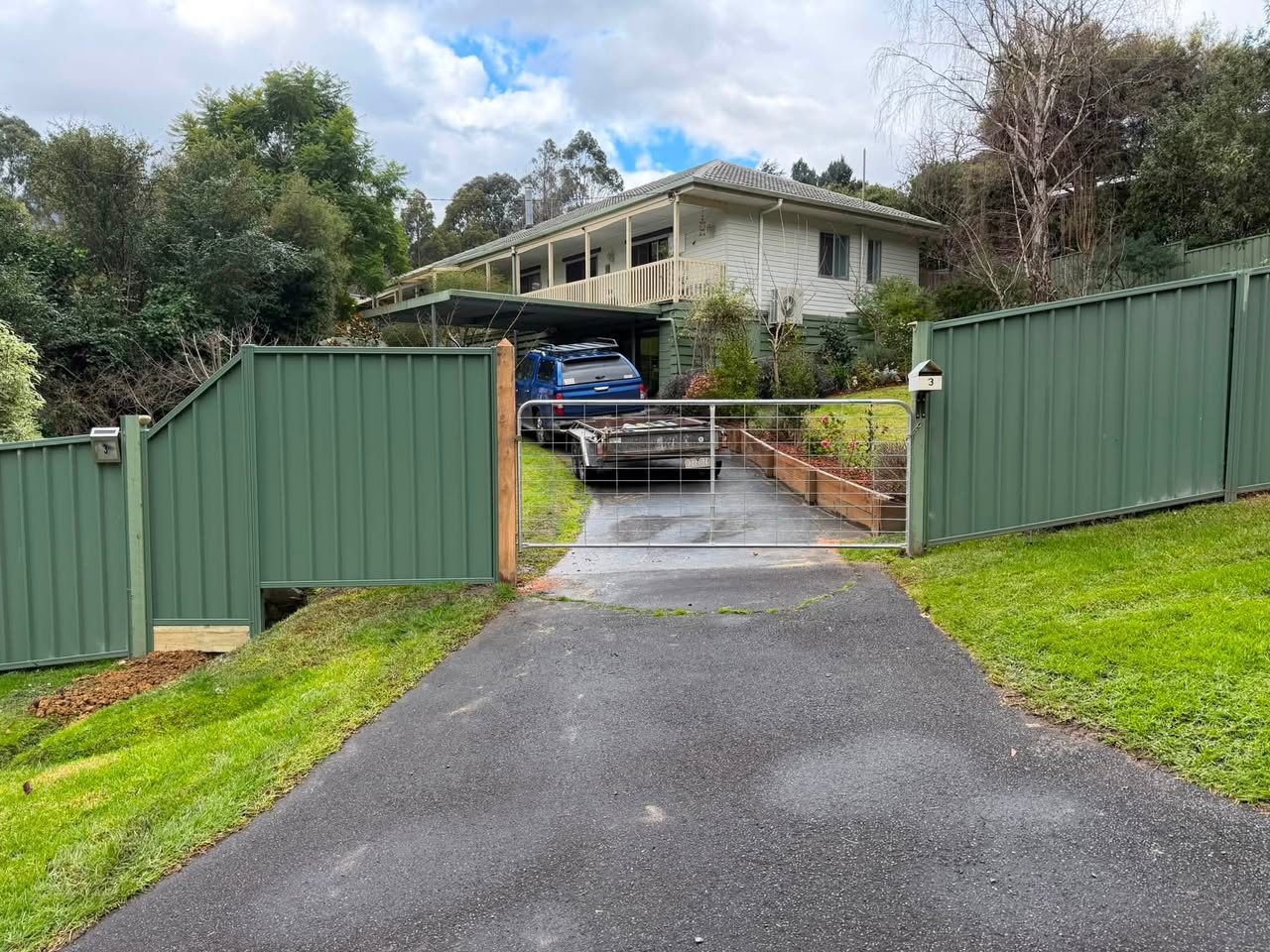 Completed green fence and wire driveway gate with a timber gate post